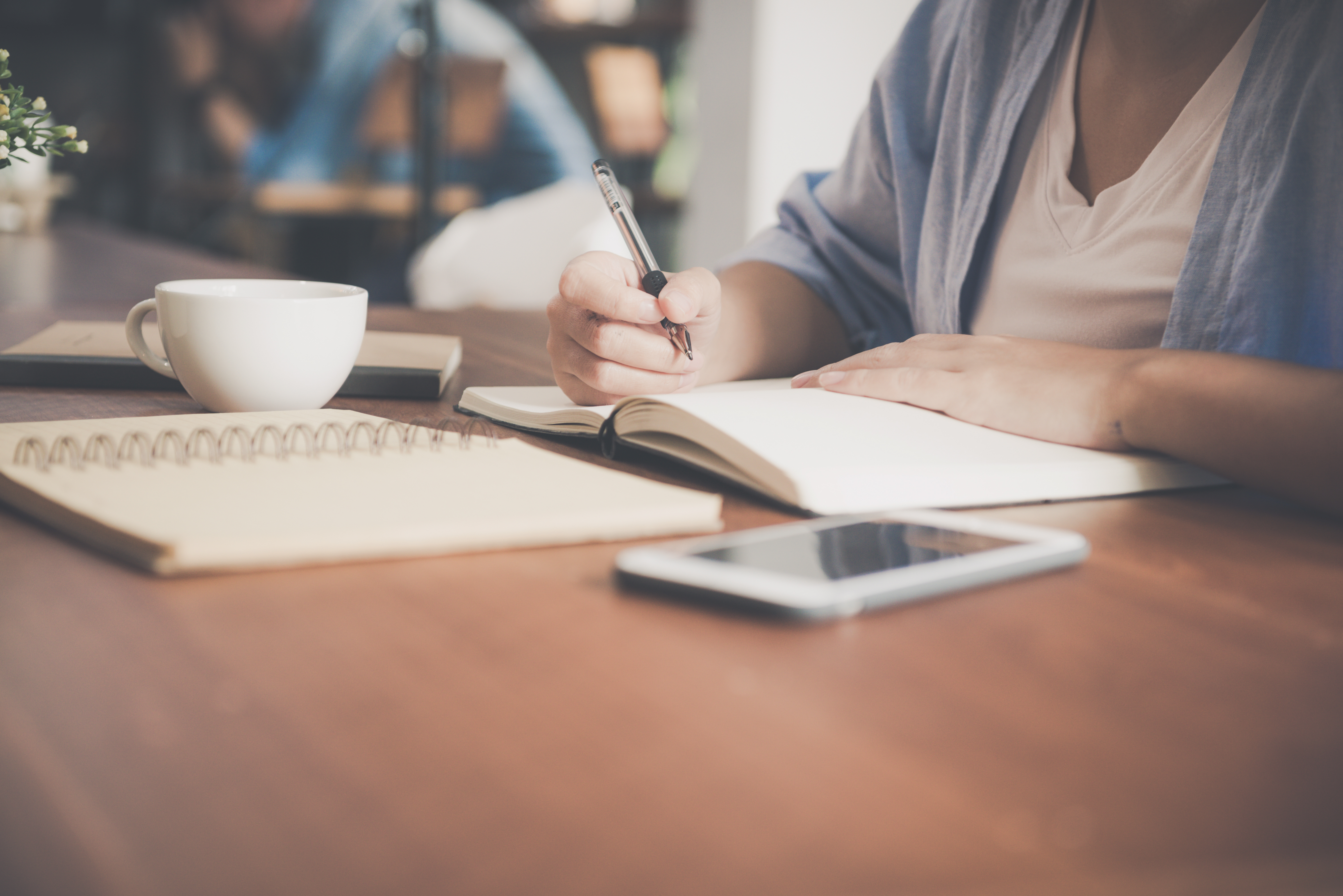 woman-writing-on-a-notebook-beside-teacup-and-tablet-733856